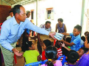A Kinship Leader in Cambodia hands packets of food to a smiling child.
