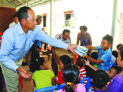 A Kinship Leader in Cambodia hands packets of food to a smiling child.