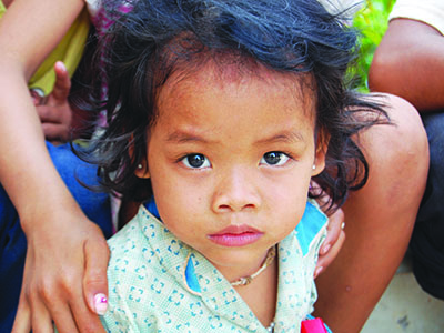 A serious young girl from Cambodia looks straight into the camera.