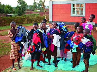 A group of young kids excitedly hold bundles of new clothes in their hands