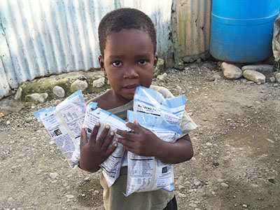 A young boy from the Dominican Republic stands holding Manna Pack food packets generously donated by Feed My Starving Children.