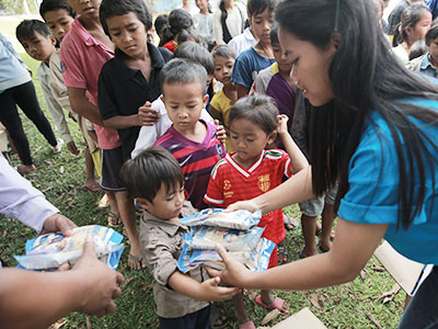 Young woman in Cambodia hands Manna Pack food packets from Feed My Starving Children to a young boy