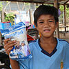 Young boy in Cambodia holds up food packet and smiles