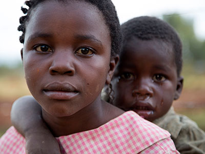 A serious young girl holds a crying baby on her back