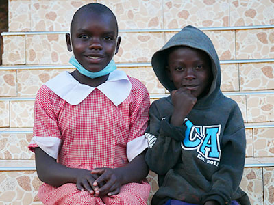 Young brother and sister sit next to each other smiling