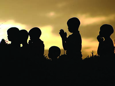 Silhouettes of children praying in front of a sunset