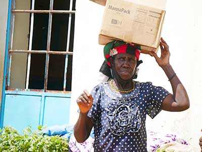 A woman in Kenya carries a box of meals on her head