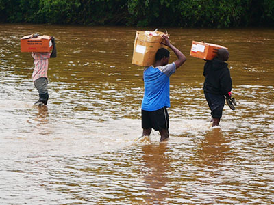 Men walk across a flooded river with boxes on their shoulders