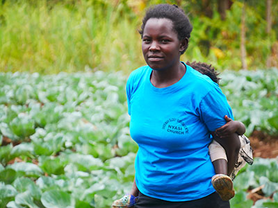 A woman stands in a garden looking solemnly at the camera