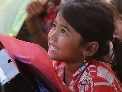 A smiling girl in Cambodia holding her new school supplies