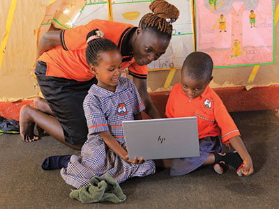 A teacher excitedly looks over the shoulders of her student using their new laptop
