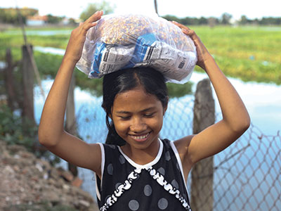 A smiling girl carrying food on her head