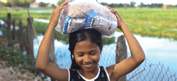 A smiling girl carrying food on her head
