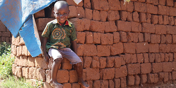 A smiling child sitting on a wall of bricks