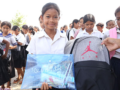 A smiling young girl holds her new backpack and school supplies