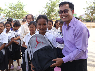 A smiling young girl holds her new backpack and school supplies