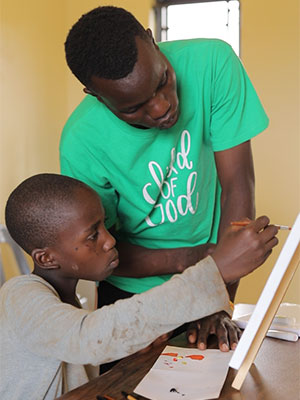 Mathias helps a younger child with their painting.