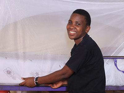 A smiling young woman in Uganda making her bed