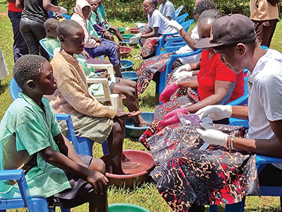 Community members sit with their feet in water during their jigger treatments