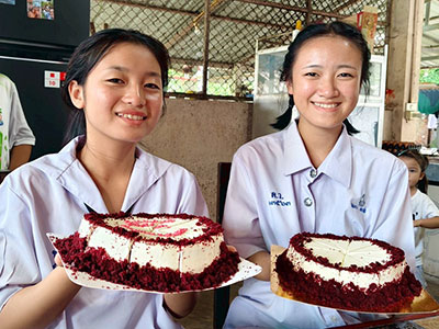 Two smiling young women in Thailand holding their birthday cakes.